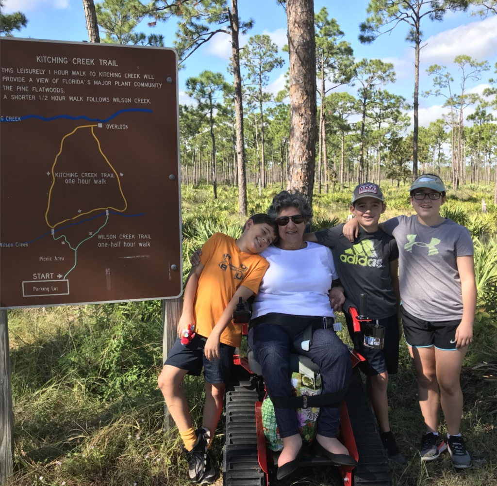 A photo of a woman using the free all-terrain track chair in Jonathan Dickinson State Park, photographed with three children