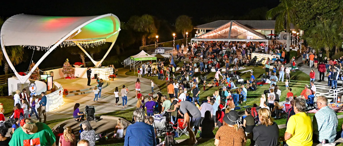 Large outdoor community event at night with people gathered near a tent and stage.