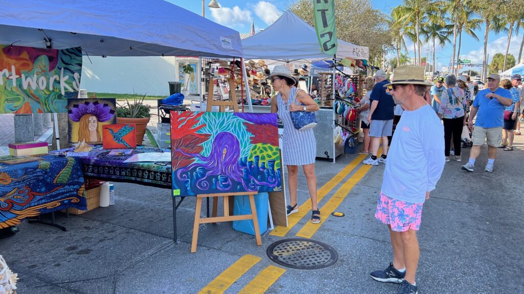 Group of attendees admiring art stalls at art show.